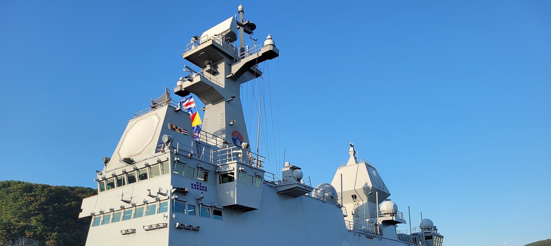 The mast and radars of a navy ship alongside at a shipyard